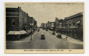 Vintage black and white image of Main Street in Fond du Lac, Wisconsin, showcasing early 20th-century storefronts, streetcars, and pedestrians.