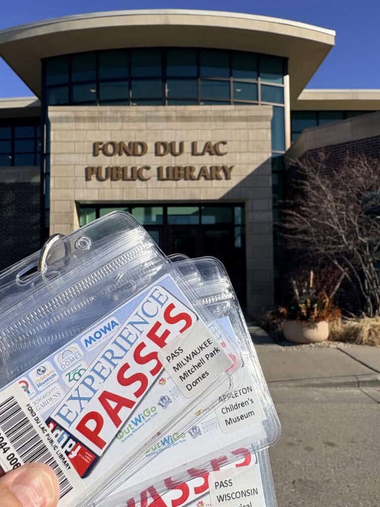 Three cards labeled "Experience Passes" are fanned out in front of a building with the words "Fond du Lac Public Library" on the front of it.
