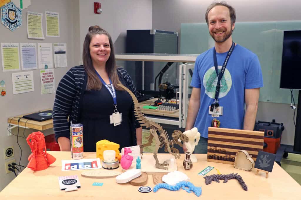 A man and a woman stand behind a table covered with various items created in the Idea Studio