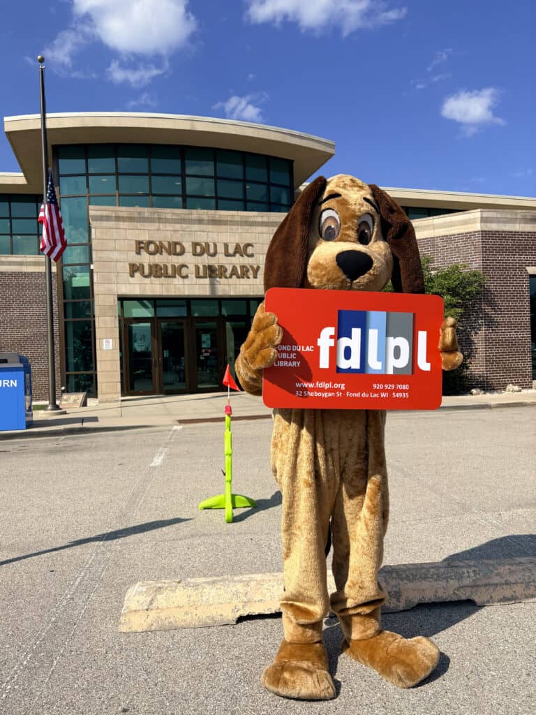A mascot holds an oversized Fond du Lac Public Library card outside of the library.